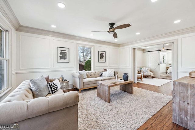 living room with crown molding, dark wood finished floors, a decorative wall, and a barn door