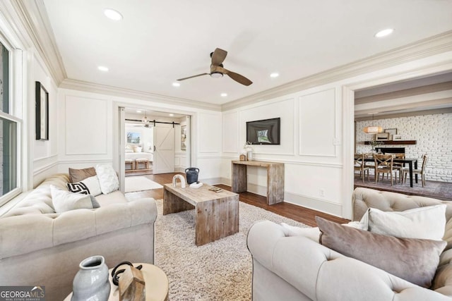 living room featuring a decorative wall, a barn door, ornamental molding, a ceiling fan, and wood finished floors