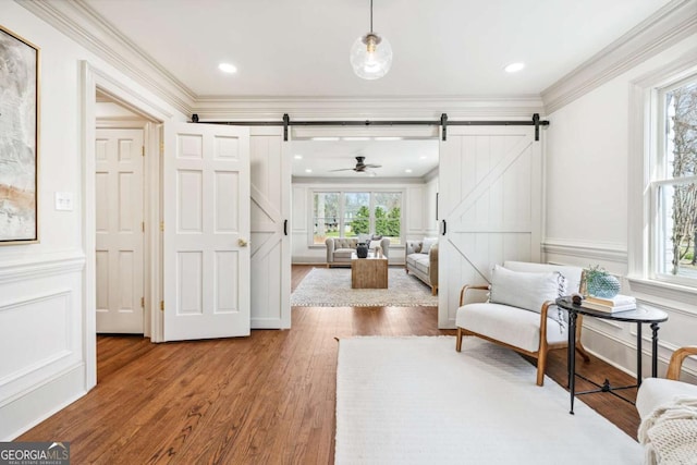 living area featuring a barn door, a decorative wall, crown molding, and wood finished floors