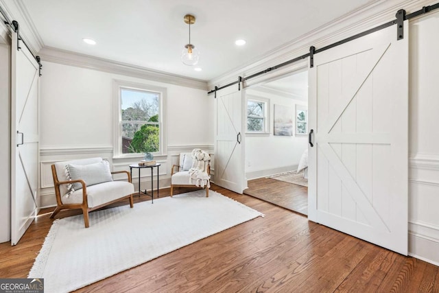 sitting room with ornamental molding, wood finished floors, wainscoting, and a barn door