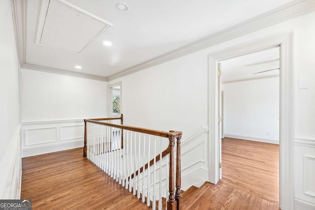 hall featuring attic access, light wood-style flooring, crown molding, an upstairs landing, and a decorative wall