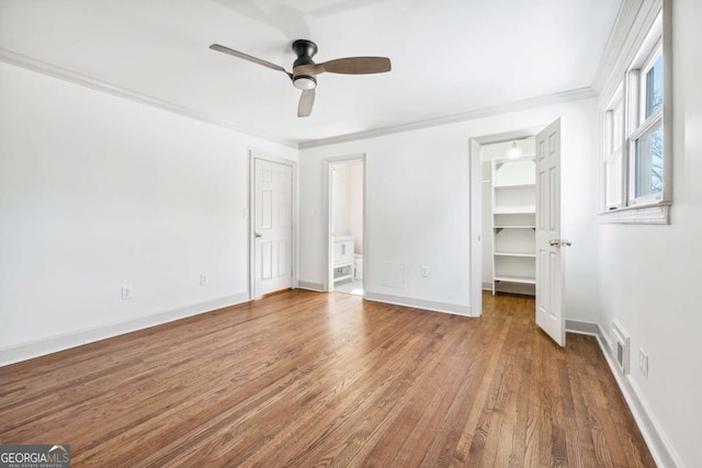 unfurnished bedroom featuring baseboards, visible vents, wood finished floors, a spacious closet, and crown molding