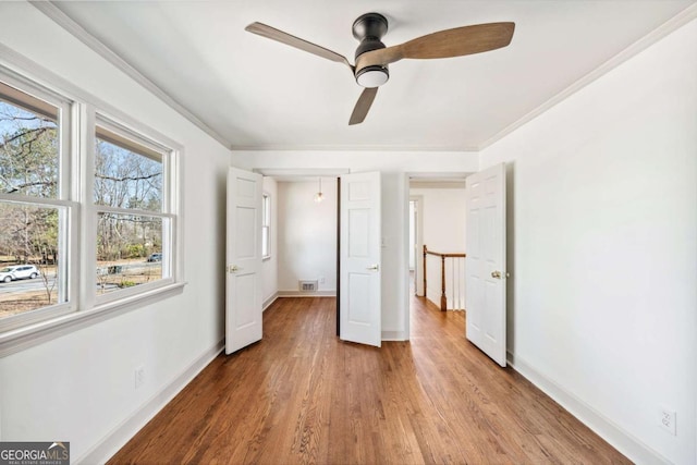 unfurnished bedroom featuring visible vents, baseboards, wood finished floors, and ornamental molding