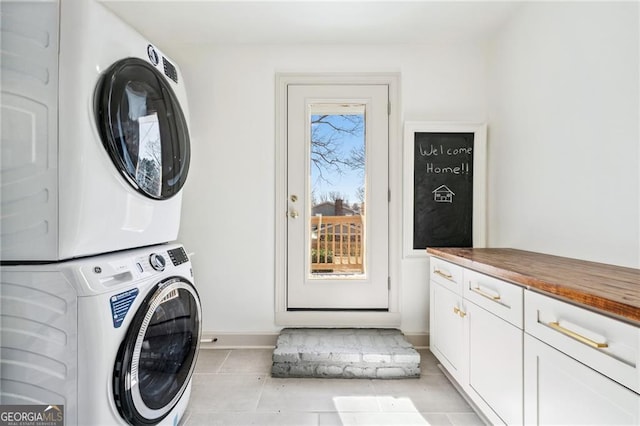 washroom with stacked washer / drying machine, cabinet space, baseboards, and light tile patterned floors