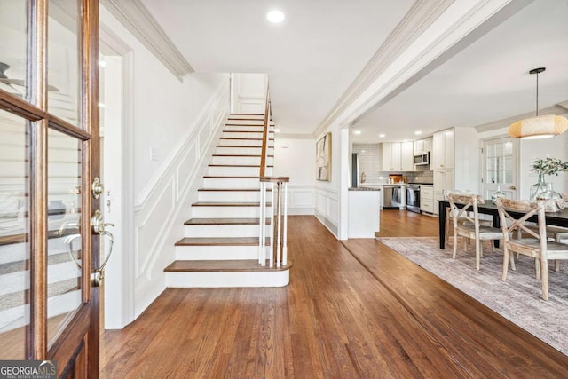 entrance foyer featuring dark wood-style floors, stairs, a decorative wall, and crown molding