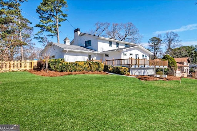 rear view of house with fence, a chimney, a wooden deck, and a lawn