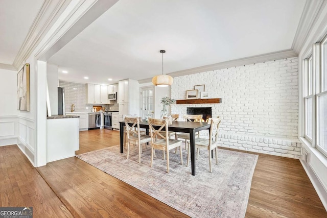 dining area with brick wall, ornamental molding, wood finished floors, and a decorative wall