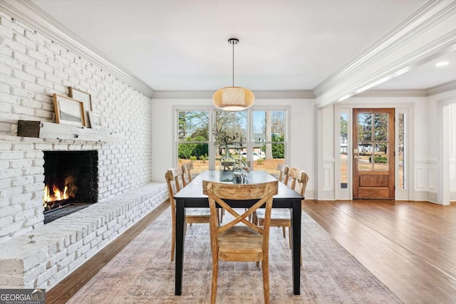 dining room with ornamental molding, a brick fireplace, and wood finished floors