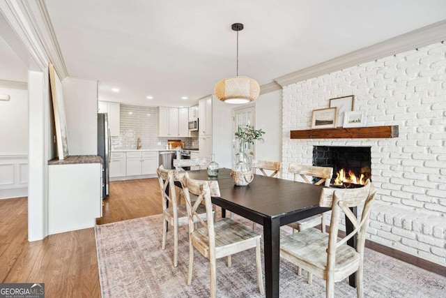 dining room featuring a decorative wall, ornamental molding, wainscoting, light wood-type flooring, and a brick fireplace