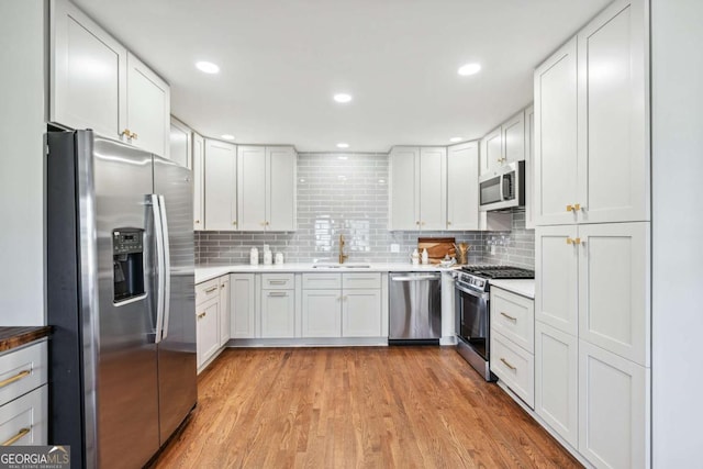 kitchen featuring appliances with stainless steel finishes, a sink, light wood-style flooring, and tasteful backsplash