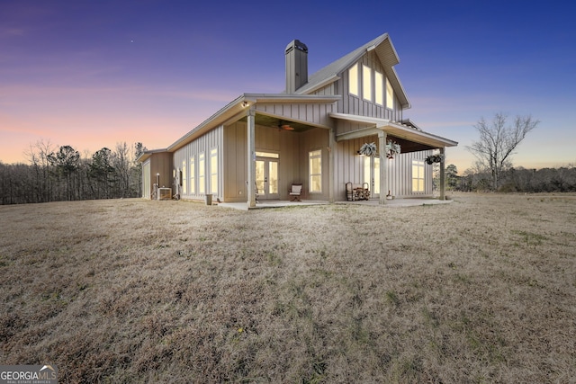 back of house at dusk with a patio, french doors, board and batten siding, and a chimney