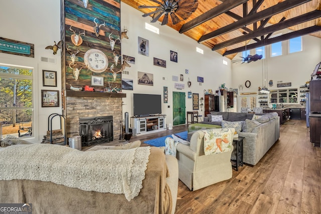 living room with a stone fireplace, visible vents, a ceiling fan, beam ceiling, and wood-type flooring