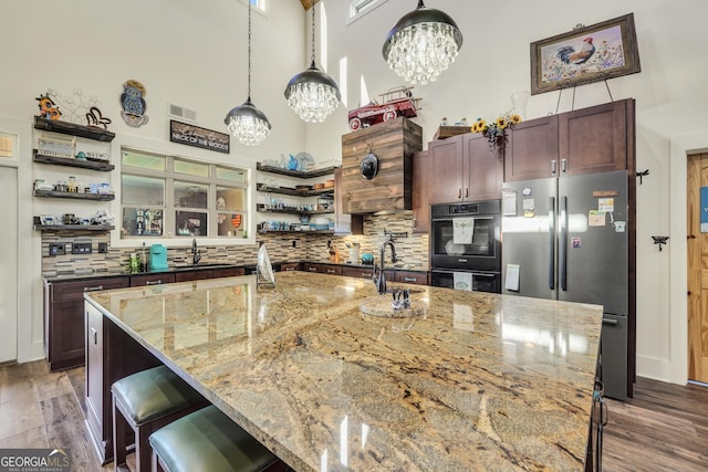 kitchen with wood finished floors, a towering ceiling, a sink, freestanding refrigerator, and open shelves