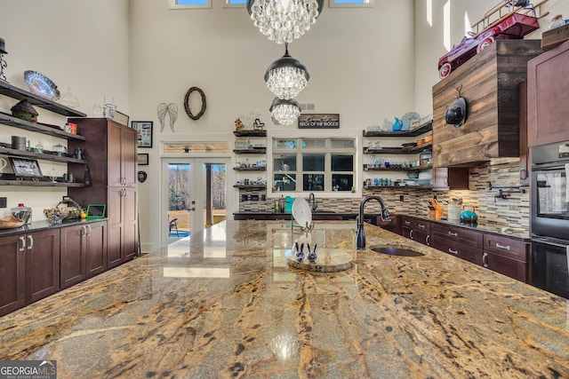 kitchen with a towering ceiling, open shelves, and a notable chandelier