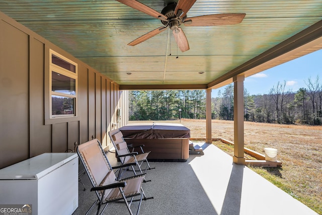 view of patio with ceiling fan, a wooded view, and a hot tub