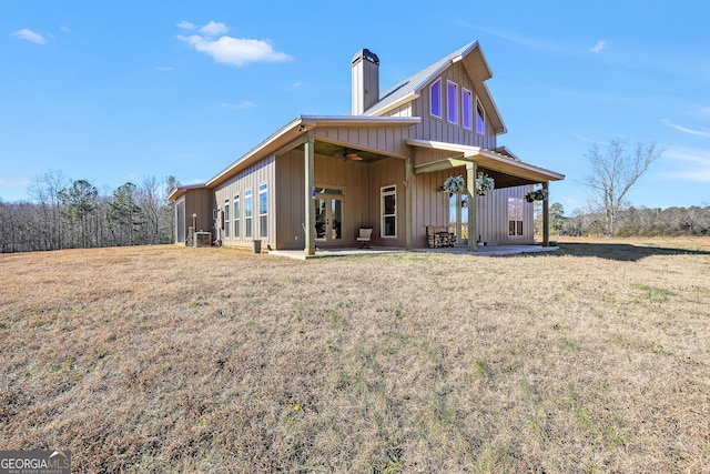 back of property with a patio area, a yard, board and batten siding, and a chimney