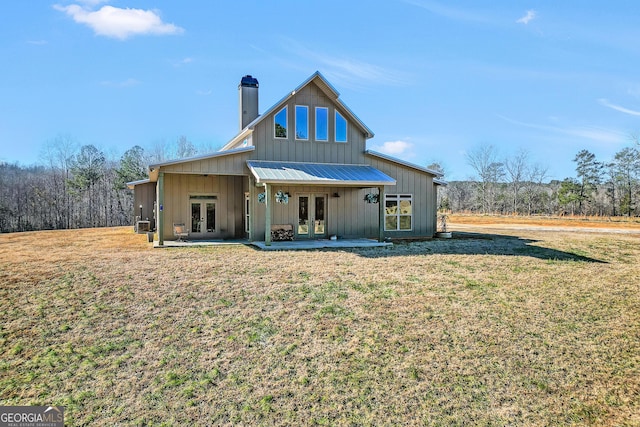 back of property with a yard, french doors, a chimney, and board and batten siding