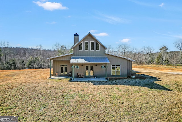 rear view of property with a lawn, a forest view, a chimney, french doors, and board and batten siding