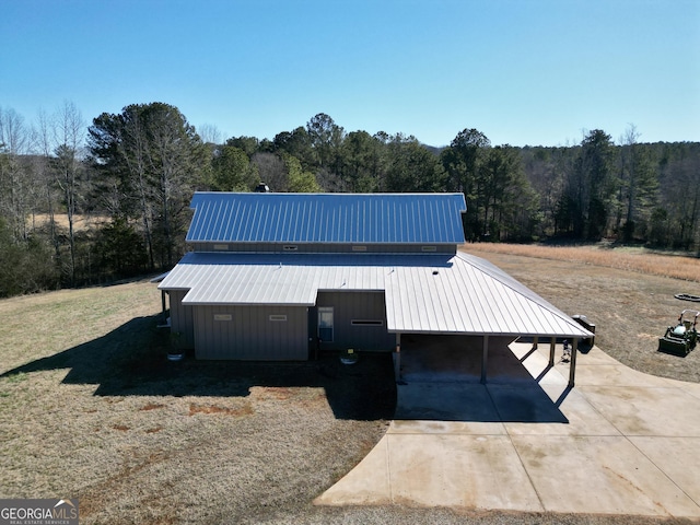 view of front facade with concrete driveway, metal roof, and a wooded view