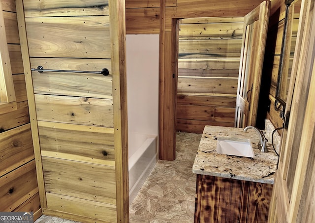 bathroom featuring a tub to relax in, vanity, and wooden walls