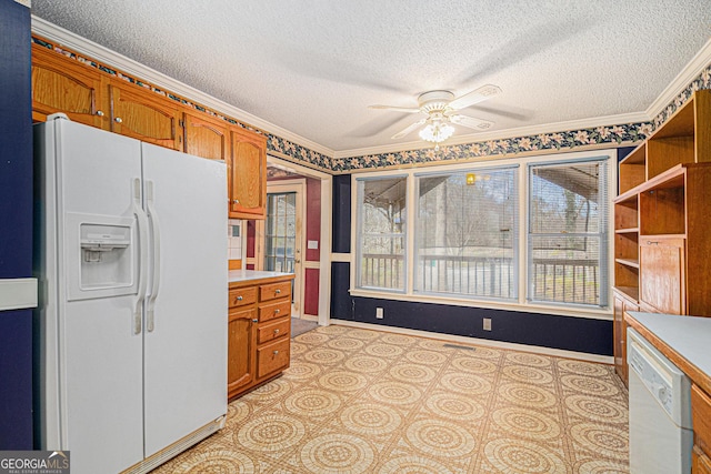 kitchen featuring light countertops, brown cabinetry, a textured ceiling, white appliances, and baseboards