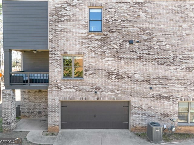 view of side of home featuring brick siding, concrete driveway, an attached garage, central AC unit, and a balcony