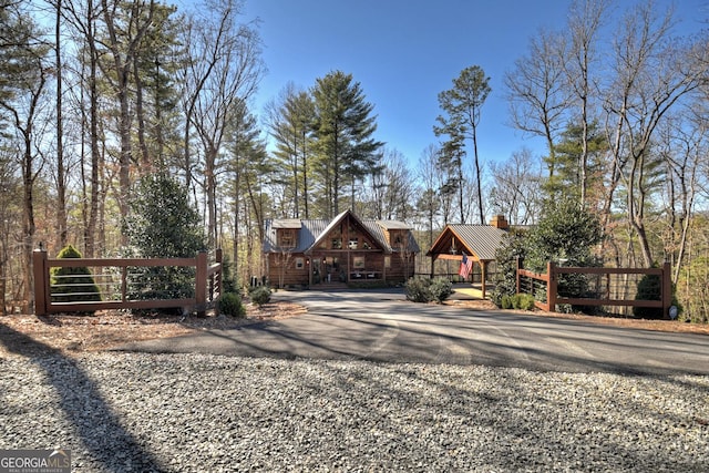 view of front of home featuring gravel driveway, a gate, a chimney, and metal roof