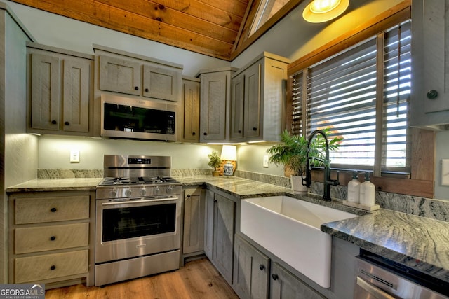 kitchen with light wood finished floors, wood ceiling, light stone counters, stainless steel appliances, and a sink