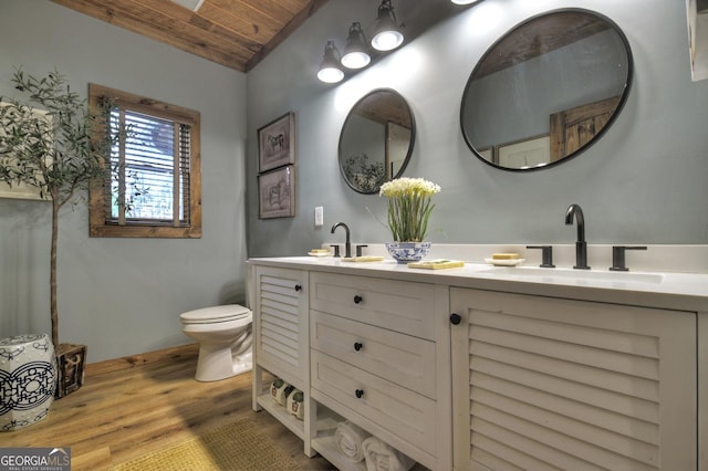 full bath with double vanity, toilet, wood ceiling, a sink, and wood finished floors