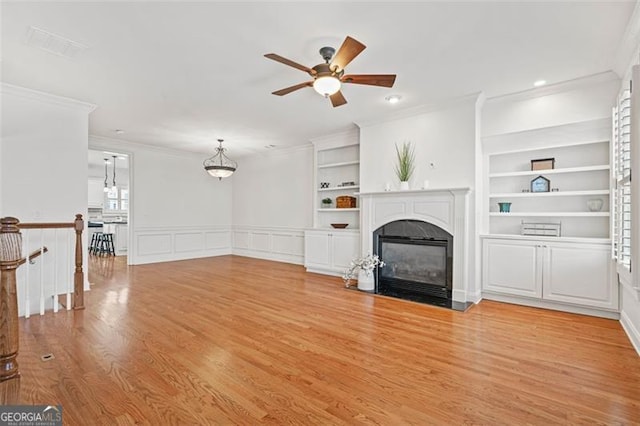 unfurnished living room with light wood-type flooring, a fireplace with flush hearth, built in features, and crown molding