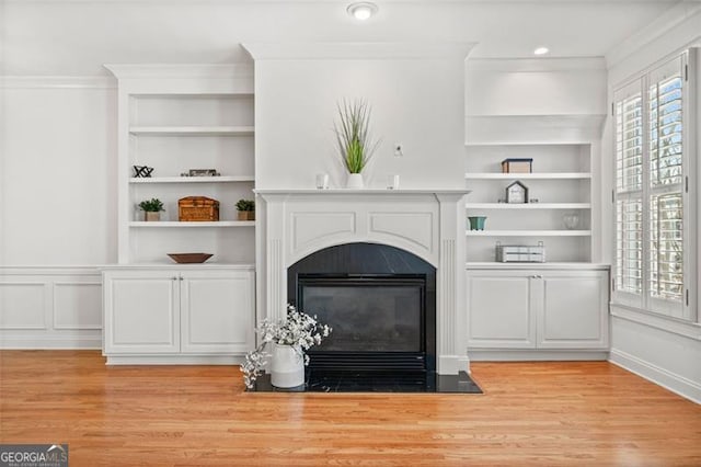 unfurnished living room featuring light wood-type flooring, a fireplace with flush hearth, built in shelves, and crown molding