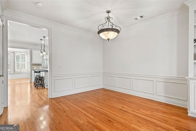 empty room with light wood finished floors, visible vents, and ornamental molding