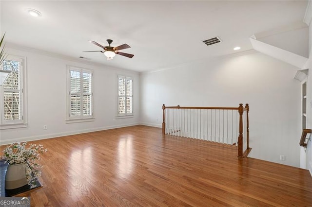 empty room featuring baseboards, visible vents, a ceiling fan, wood finished floors, and crown molding