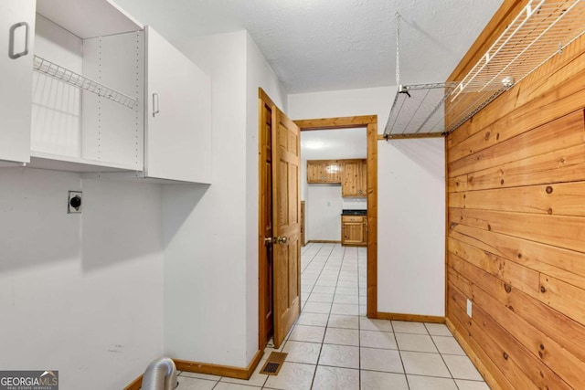 clothes washing area with cabinet space, light tile patterned floors, wooden walls, baseboards, and hookup for an electric dryer