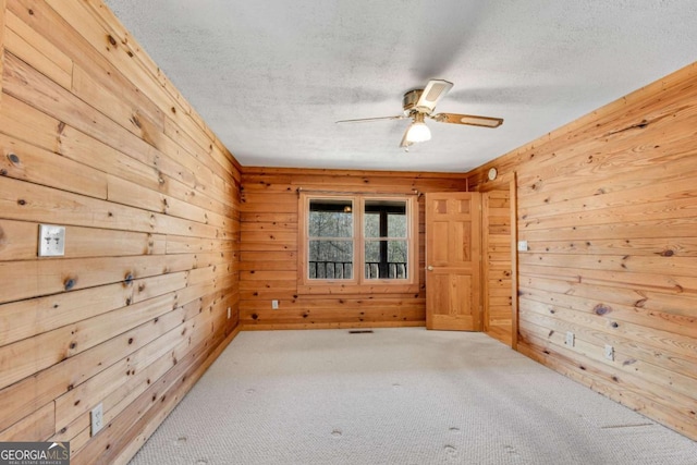 carpeted empty room featuring wooden walls, ceiling fan, and a textured ceiling