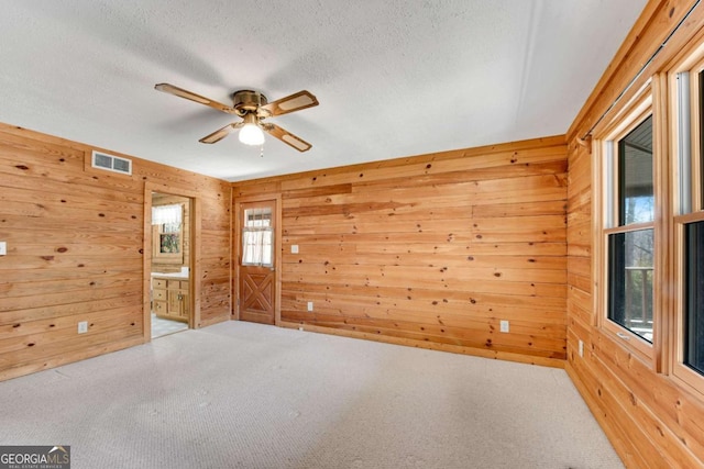 empty room featuring carpet, visible vents, wood walls, a textured ceiling, and ceiling fan