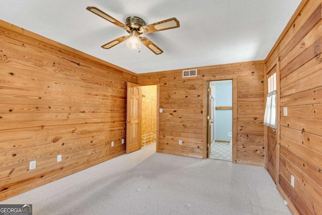 empty room with wood walls, carpet, visible vents, and a ceiling fan