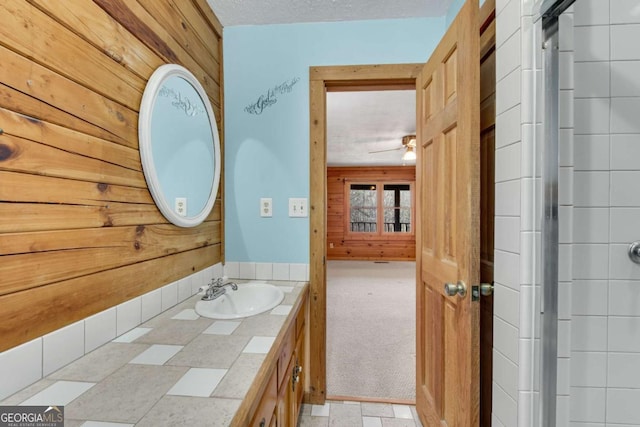 bathroom featuring ceiling fan, wooden walls, a textured ceiling, and vanity