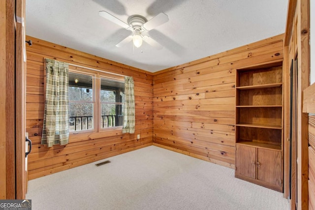 carpeted empty room with ceiling fan, wood walls, a textured ceiling, and visible vents