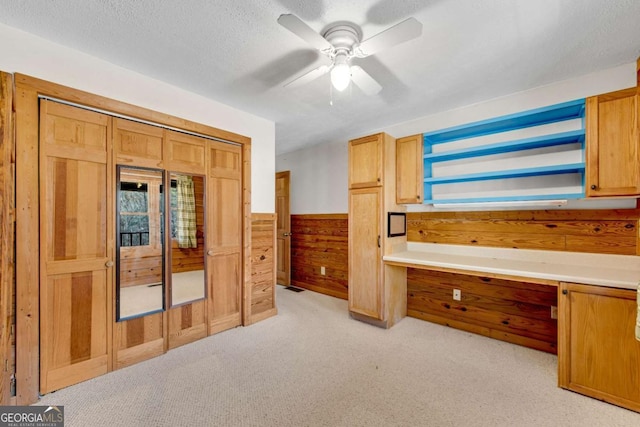 office featuring light colored carpet, a wainscoted wall, a textured ceiling, wood walls, and built in desk