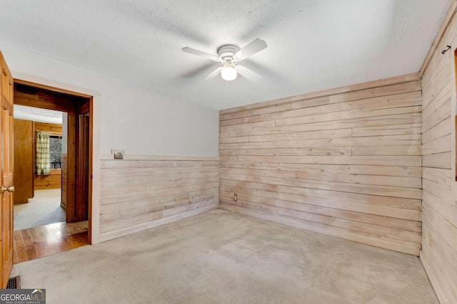 empty room with a ceiling fan, wood walls, and a textured ceiling