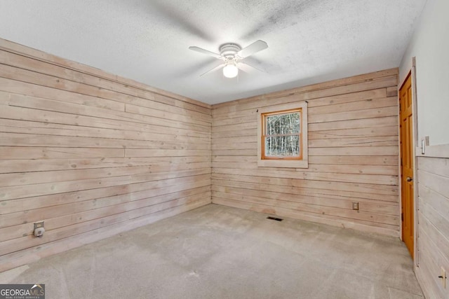 spare room with a textured ceiling, carpet, a ceiling fan, and wooden walls