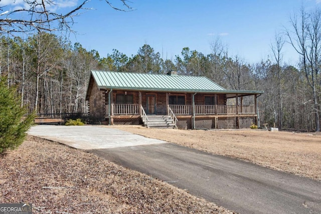 log-style house with metal roof, covered porch, a forest view, log exterior, and a standing seam roof