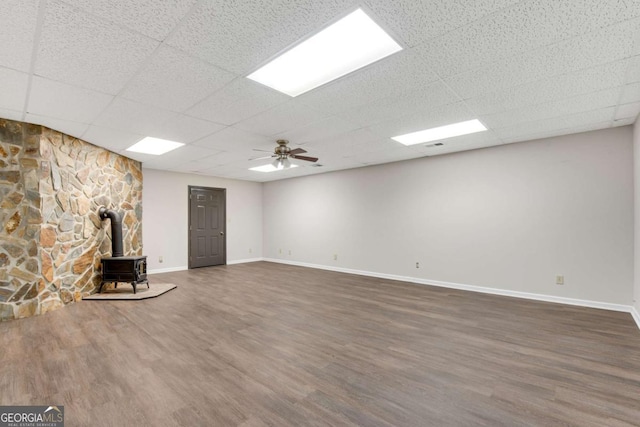 unfurnished living room featuring dark wood-type flooring, a drop ceiling, a wood stove, and baseboards