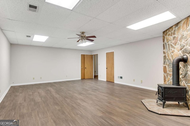 unfurnished living room featuring baseboards, visible vents, ceiling fan, wood finished floors, and a wood stove