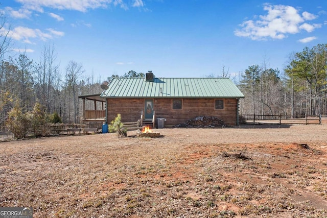 back of property featuring an outdoor fire pit, a chimney, metal roof, a standing seam roof, and cooling unit