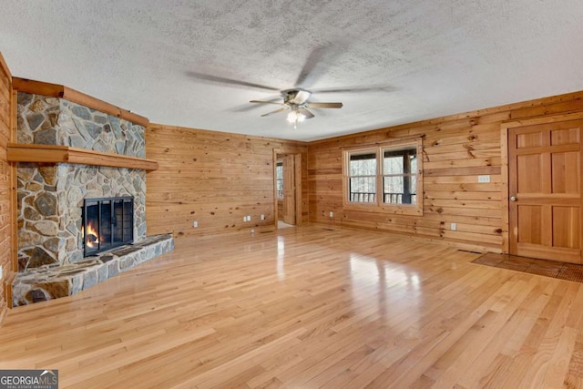 unfurnished living room with wooden walls, a ceiling fan, wood finished floors, a textured ceiling, and a fireplace