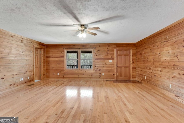 spare room featuring a textured ceiling, light wood finished floors, a ceiling fan, and wooden walls