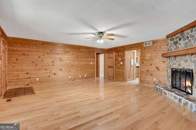 unfurnished living room with light wood-type flooring, visible vents, a fireplace, and a textured ceiling