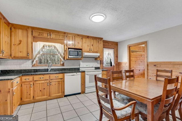 kitchen with dark countertops, light tile patterned flooring, a sink, white appliances, and under cabinet range hood